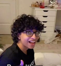 a woman with curly hair wearing glasses and giving the thumbs up sign in front of her