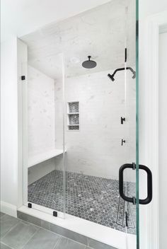 a walk in shower sitting next to a white wall and tiled floor with black accents