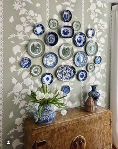 a wall with many plates on it and a vase in front of the plate display