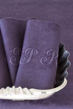 three purple napkins with monogrammed initials on them in a silver dish holder