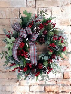 a wreath with red flowers and pine cones hanging on a brick wall