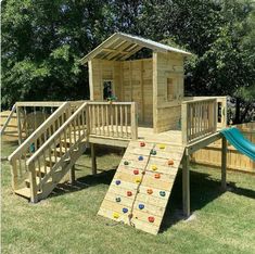 a wooden play structure with a slide and climbing wall in the back yard for children