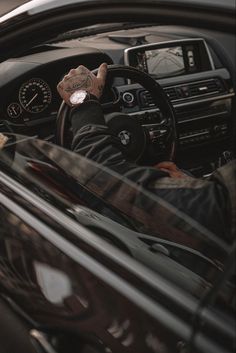 a man driving a car with his hands on the steering wheel while wearing a black jacket