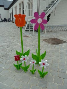 three paper flowers sitting on top of a brick floor next to a white building with stairs