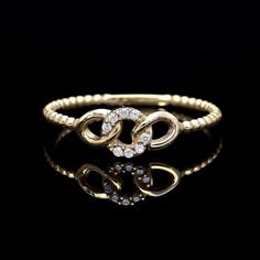 a gold ring with two intertwined hearts and white diamonds on the side, against a black background