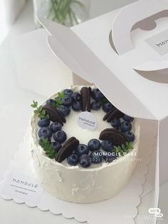 a white cake with blueberries and oreo cookies on top is in a box