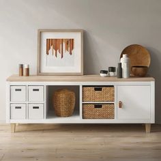 a white cabinet with baskets on it and a painting hanging above the drawers in front of it