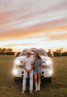 a man and woman sitting on the back of a truck in a field at sunset