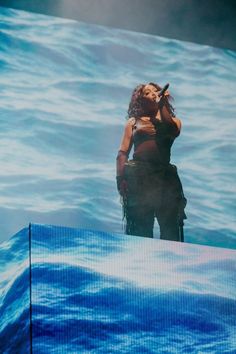 a woman standing on top of a stage in front of a large screen with water