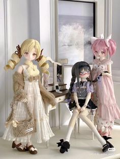 three dolls are posed together in front of a table and chair, one is sitting on the floor