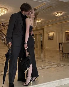 a man and woman standing next to each other in front of a staircase with chandeliers