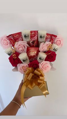 a hand holding a bouquet of roses and creams with a gold ribbon around it