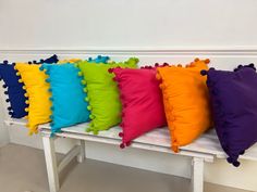 four different colored pillows on a white bench