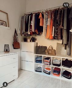 an organized closet with clothes and handbags hanging on the wall, along with white drawers