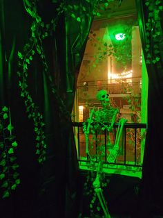 a skeleton sitting on a balcony in the dark with green light coming from behind it