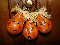 three orange pumpkins with faces painted on them hanging from a doorknotp