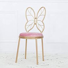 a gold chair with a pink seat and butterfly shaped back rests against a white wall