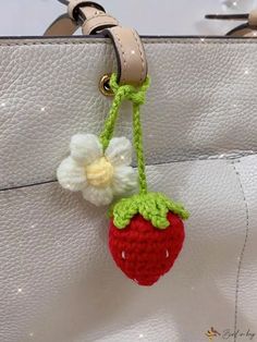 a crocheted strawberry hanging from a white purse with a flower attached to it