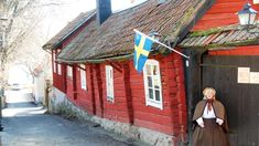 a woman standing in front of a red building with a swedish flag hanging from the roof