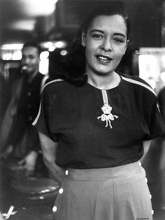 black and white photograph of a woman standing in front of a building with her hands on her hips