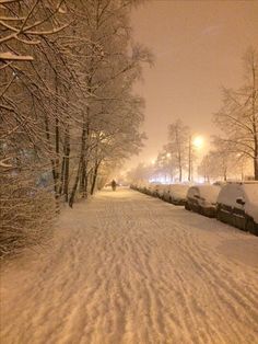 a snow covered street with cars parked on the side and people walking in the distance