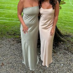 two women standing next to each other in front of a tree and grassy area with trees