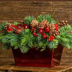 a potted plant with pine cones, berries and evergreens on it sitting on a wooden table