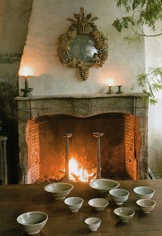 there are many bowls on the table in front of the fire place with candles burning