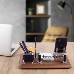 a desk with a cell phone, pen and pencil holder on it next to a laptop