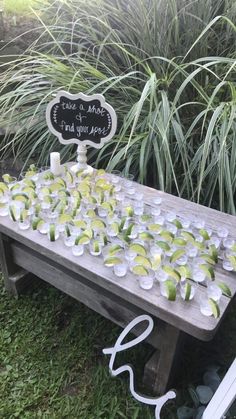 a wooden table topped with cups filled with watermelon and lemons next to tall grass