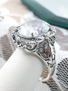 Oval Gem Sterling Silver Filigree RingBeauty Design#D229 Introducing the magnificent D229 Beauty Ring, a brand-new Vintage reproduction sterling silver filigree ring. The perfect oval-cut simulated gemstone of high quality is a jaw-dropping sight. The gemstone is 12mm by 10mm (just shy of 3/8" inch) in size, while the ring itself is 5/8th of an inch (16.5mm) in length and sits 7mm off the finger. This exquisite rendition of a Gothic design filigree ring is one of a kind and is sure to make heads Diamond White Oval Topaz Wedding Ring, Oval Diamond White Topaz Ring For Wedding, Oval Diamond White Topaz Wedding Ring, Vintage White Rings With Accent Stones, Diamond White Oval Crystal Ring With Accent Stones, White Diamond Crystal Ring With Oval Shape, Formal White Topaz Ring With Cubic Zirconia, Oval Diamond White Crystal Ring With Accent Stones, White Oval Crystal Wedding Ring