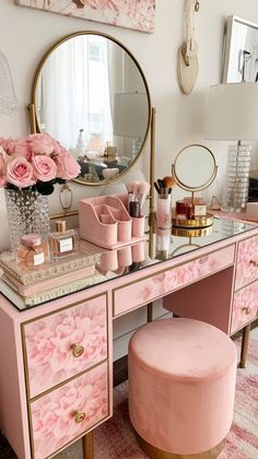 a pink vanity with gold accents and flowers on the mirror, along with a stool