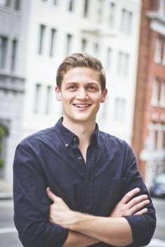 a young man standing in front of a building with his arms crossed and smiling at the camera