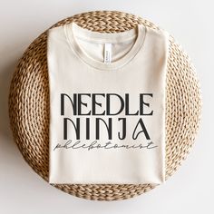 a white t - shirt that says needle ninja entertainment on it sitting on a wicker basket