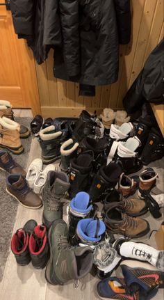 a pile of shoes sitting on top of a wooden floor next to a coat rack