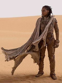 a woman with dreadlocks standing in the middle of a desert, holding a scarf