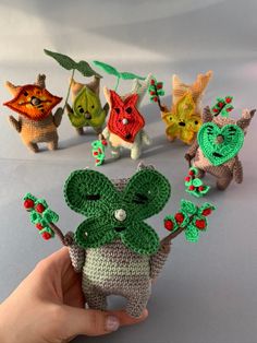 small crocheted animals are being held up by someone's hand, with the smaller ones wearing green and red