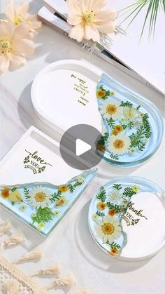 two plates with flowers on them are sitting next to a card and some other items