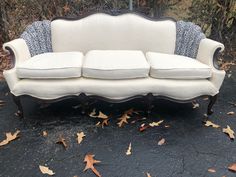 a white couch sitting on top of a black floor next to leaves and trees in the background