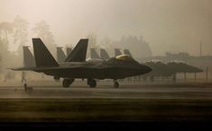 a fighter jet sitting on top of an airport tarmac next to other planes in the fog