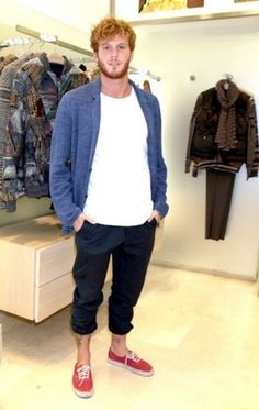 a man standing in front of a clothing rack with his hands in his pockets while wearing red shoes