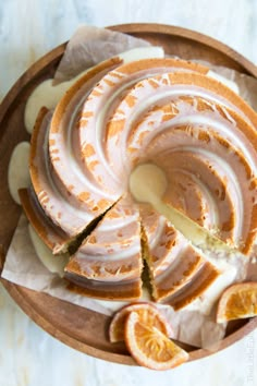 an orange cake with icing and slices cut out on a wooden platter next to sliced oranges