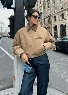 a woman standing on the side of a street next to a traffic light holding a purse