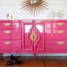 a bright pink dresser with gold accents in the middle and shoes on the floor next to it