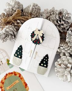 some pine cones and christmas decorations are on the table next to an open door with a bow