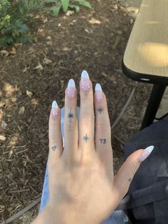 a woman's hand with white and pink nail polish on it, sitting in front of a bench