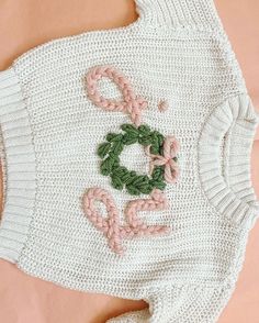 a crocheted sweater with pink flowers and green leaves on the front, sitting on top of an orange surface