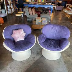 two purple chairs sitting on top of white pedestals in a room filled with furniture