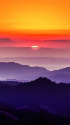 the sun is setting over some mountains in the foggy valley below, as seen from an overlook point