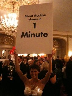 a woman holding up a sign that says silent auction closed in 1 minute at a party